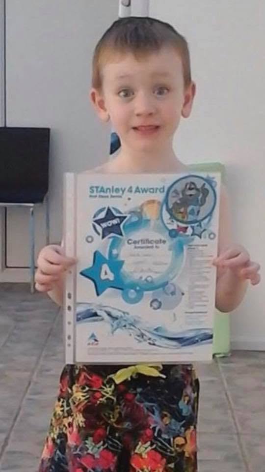 A young swimmer at the poolside holding up a STAnley 4 swimming award certificate